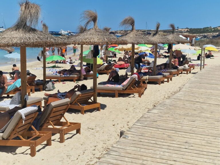 Un camarero, con visera blanca, sirve a unos turistas tumbados en una hamaca.