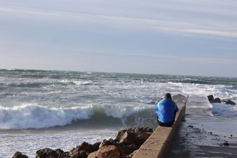 Una persona sentada frente al mar contempla el oleaje.