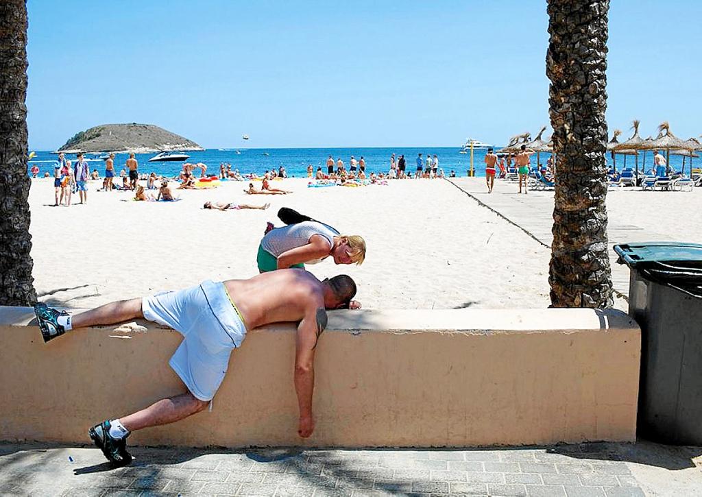 En la foto aparece una mujer que observa de cerca a un hombre que duerme la borrachera en la playa de Magaluf | Foto: Peter Dench