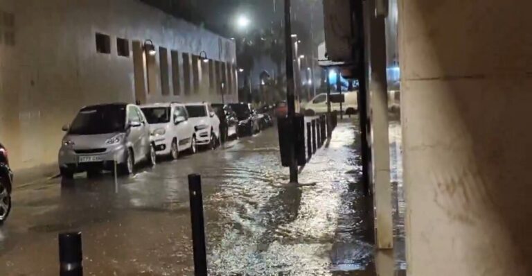 Calle inundada por lluvia intensa con coches aparcados