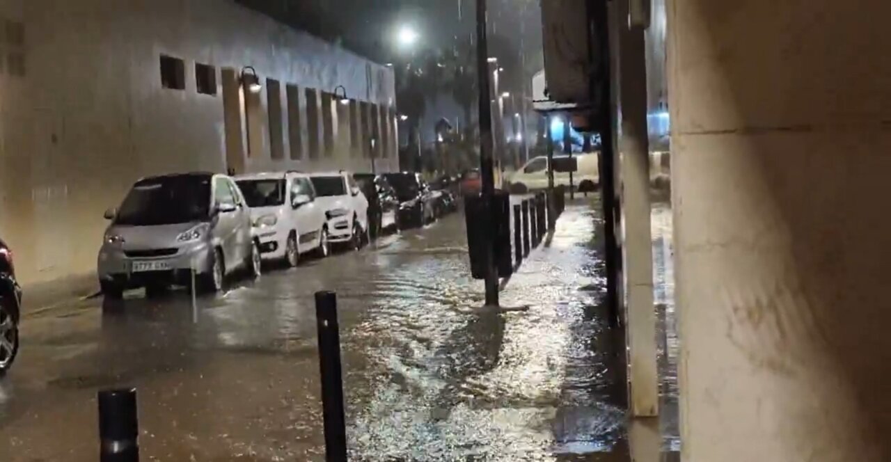 Calle inundada por lluvia intensa con coches aparcados