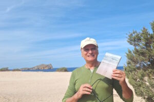 Ramon Mayol sosteniendo su libro en una playa de Ibiza
