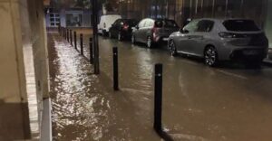 Calle inundada con vehículos estacionados y postes visibles