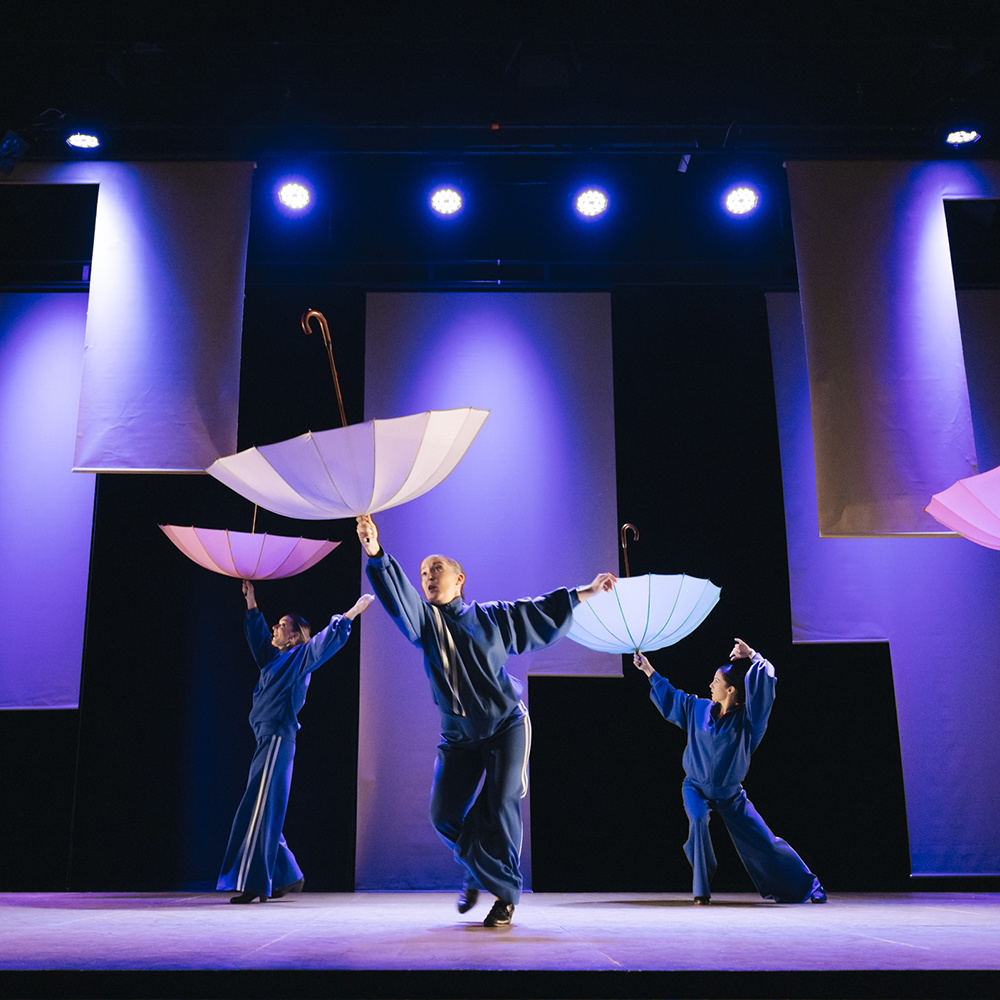 Actuación de danza con paraguas en un escenario iluminado
