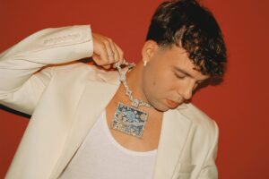 El artista canario Quevedo con un collar brillante en un fondo rojo.