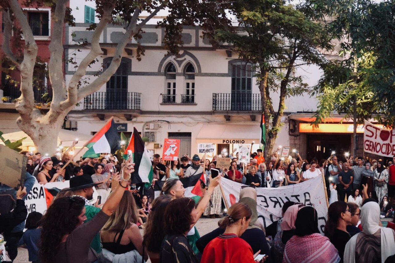 Multitud en protesta sosteniendo banderas y pancartas en un evento pacífico.