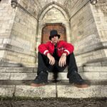 Aukan sentado en escaleras de piedra con chaqueta roja