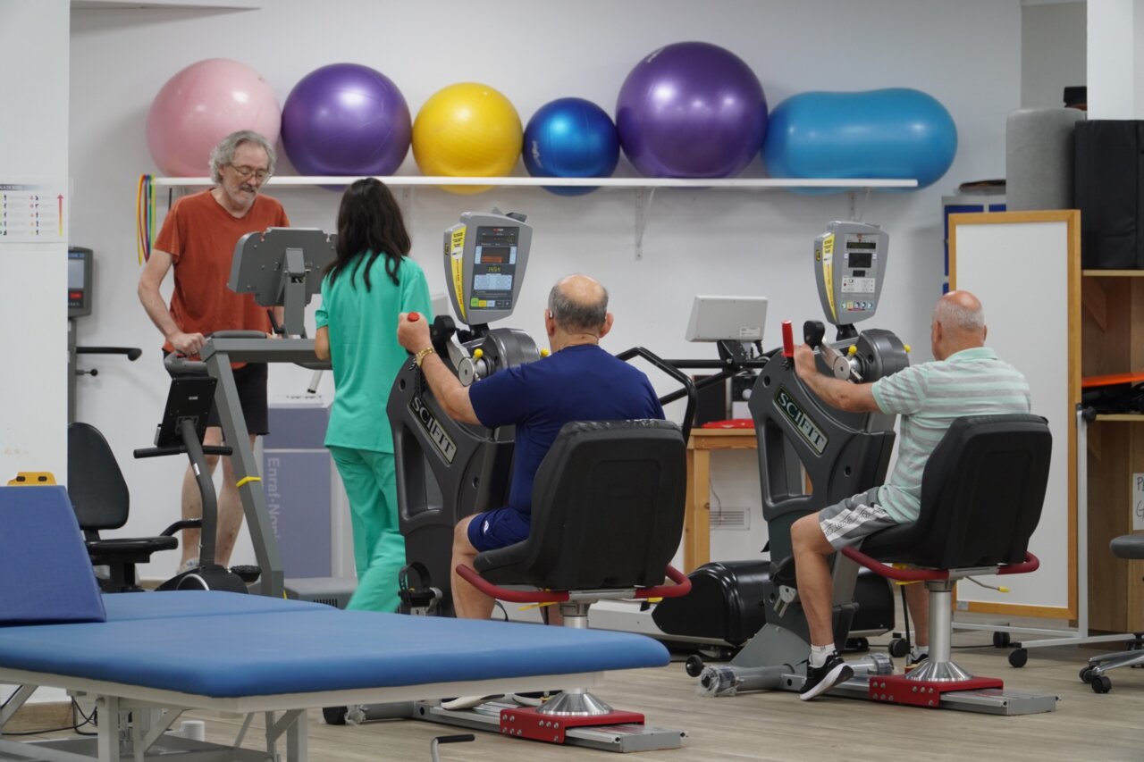 Personas realizando ejercicios en el gimnasio de AEMIF con equipos de rehabilitación.
