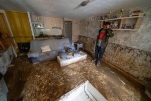 Hombre preocupado en una sala inundada con muebles dañados