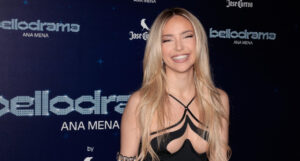 Ana Mena sonriendo en un evento con fondo azul brillante