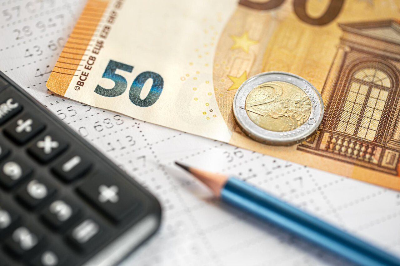 Billetes y monedas de euro sobre una hoja de cálculo y una calculadora