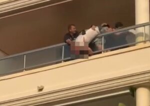 Hombre en un balcón siendo sostenido por varias personas