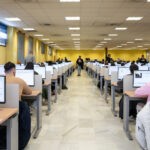 Estudiantes realizando examen teórico de conducir en aula con computadoras.