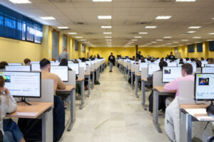 Estudiantes realizando examen te&oacute;rico de conducir en aula con computadoras.