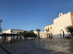 Plaza en Formentera con edificios y palmeras bajo un cielo despejado
