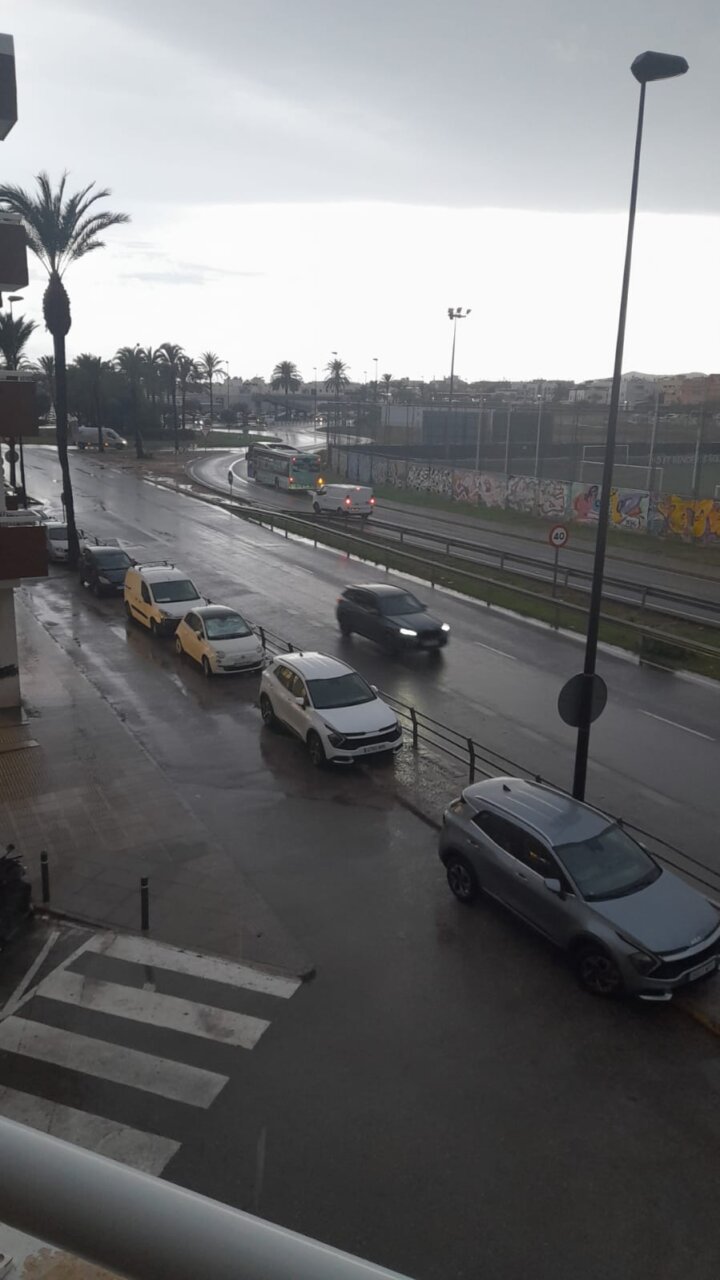 Vista de una calle en Ibiza bajo lluvia con coches estacionados.