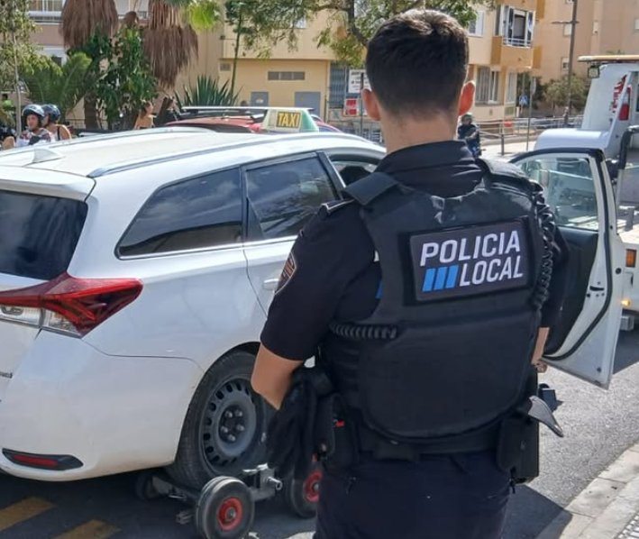 Policía local observando un vehículo blanco con un taxi al fondo