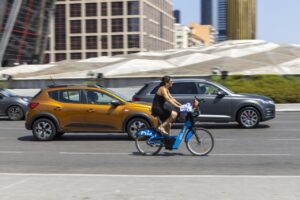 Mujer en bicicleta azul circulando entre coches en una ciudad moderna