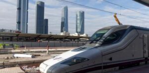 Tren de alta velocidad en una estación moderna con edificios altos al fondo.
