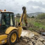 Excavadora amarilla trabajando en un terreno afectado por la lluvia.