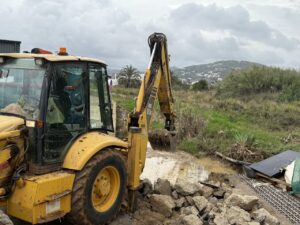 Excavadora amarilla trabajando en un terreno afectado por la lluvia.