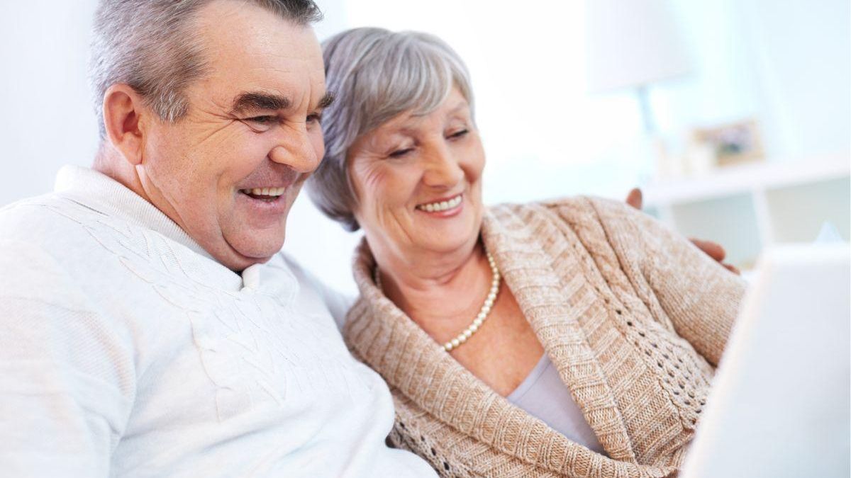 Pareja de jubilados sonriendo mientras miran una tablet