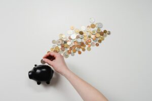 Mano colocando una moneda en una alcancía negra con monedas alrededor.
