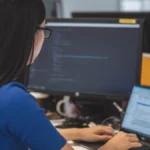 Mujer trabajando en oficina con dos computadoras